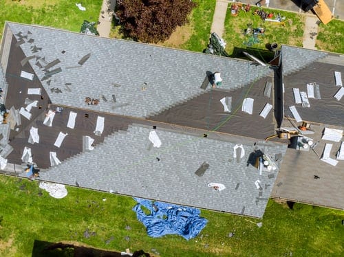 Aerial view of a residential roof renovation in progress with crews replacing decking and underlayment